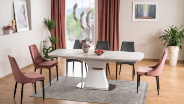 Duży stół ceramiczny w kolorze białym i tapicerowane krzesła z pikowanym siedziskiem w otwartej jadalni połączonej z salonem