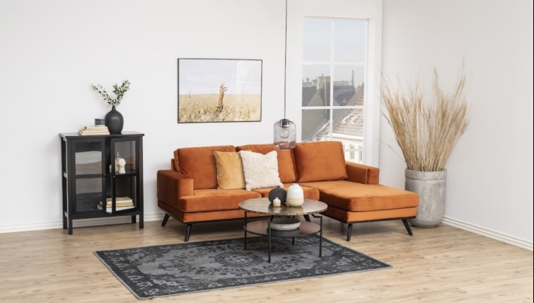Pomarańczowa kanapa narożna tapicerowana welurem w salonie z czarnymi meblami