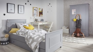 Dwudrzwiowa szafa na ubrania oraz łóżko z szufladą w pokoju chłopca z drewnianą podłogą i miejscem do nauki