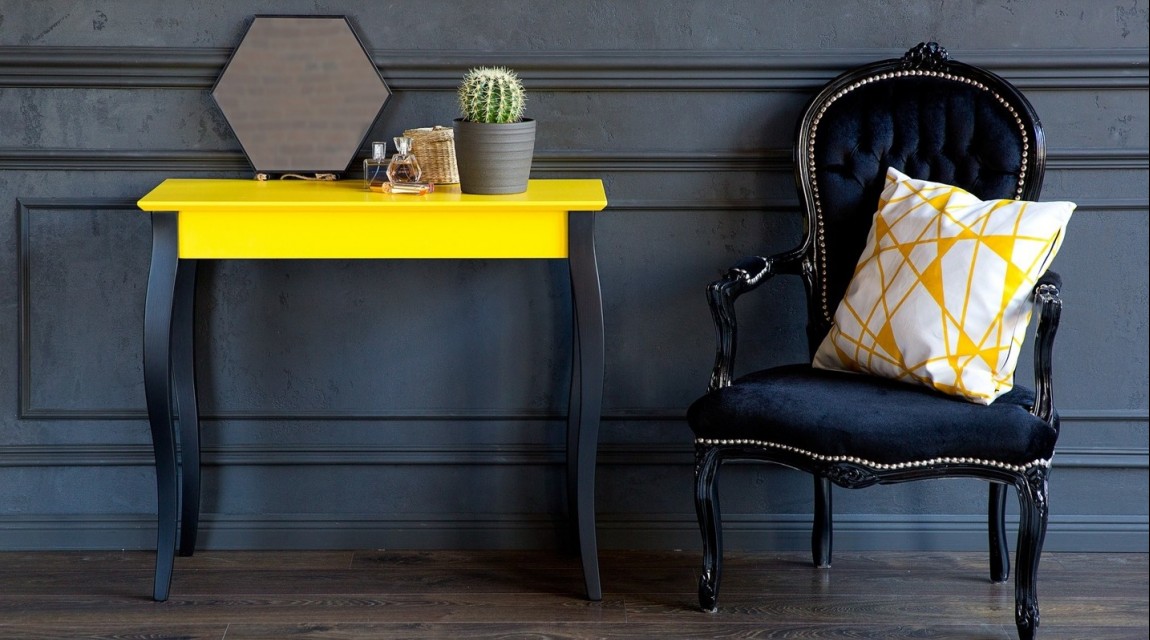 Żółta konsola na czarnych drewnianych nogach w towarzystwie czarnego fotela retro