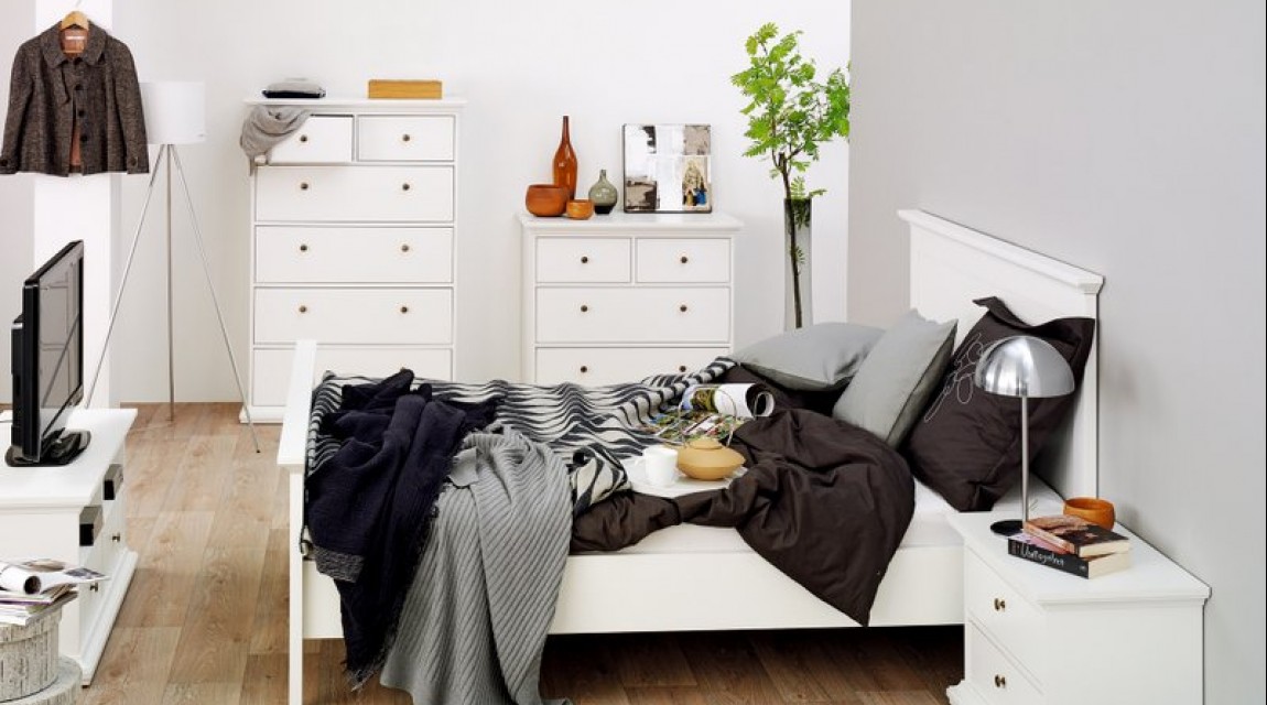 Białe łóżko z wysokim wezgłowiem uzupełnione szafką nocną oraz komody z szufladami i szafka RTV