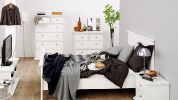 Białe łóżko z wysokim wezgłowiem uzupełnione szafką nocną oraz komody z szufladami i szafka RTV