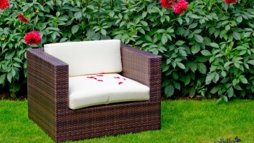 Fotel z technorattanu z miękkimi poduszkami w ogrodowej scenerii z kwitnącymi kwiatami
