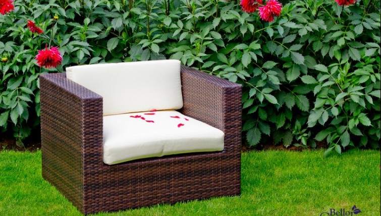 Fotel z technorattanu z miękkimi poduszkami w ogrodowej scenerii z kwitnącymi kwiatami