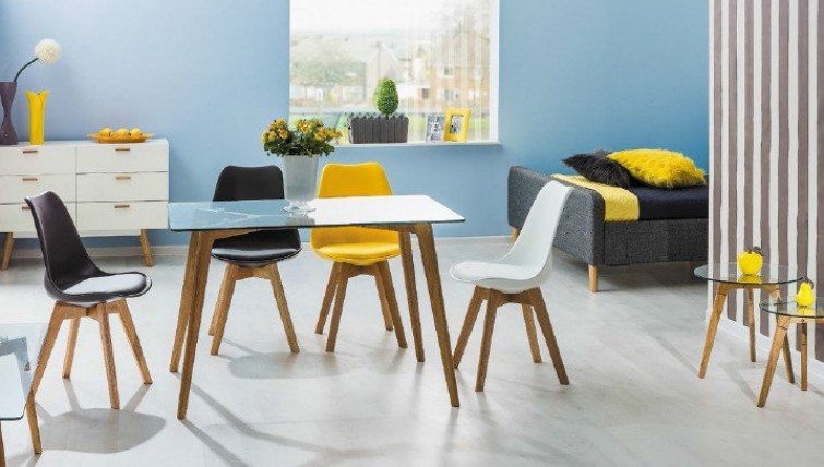 Kolorowe krzesła z ekoskóry bez podłokietników oraz stół ze szklanym blatem i drewnianymi nogami