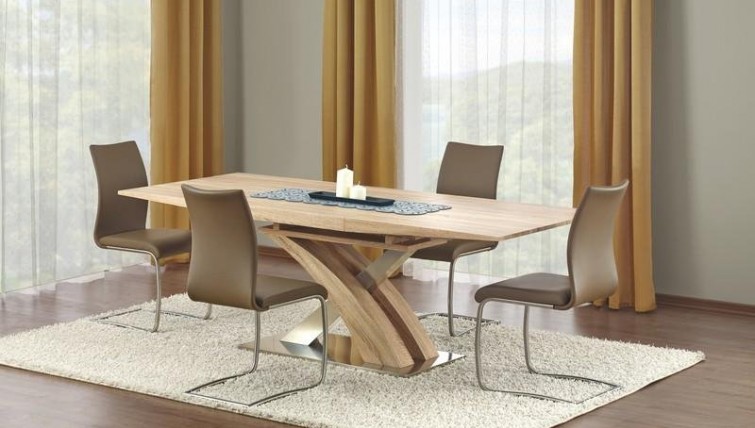 Rozkładany stół w imitacji drewna na ozdobnej nodze w towarzystwie nowoczesnych krzeseł na płozach