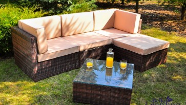 Sofa narożna z miękkimi poduchami oraz stolik ze szklanym blatem w dużym ogrodzie