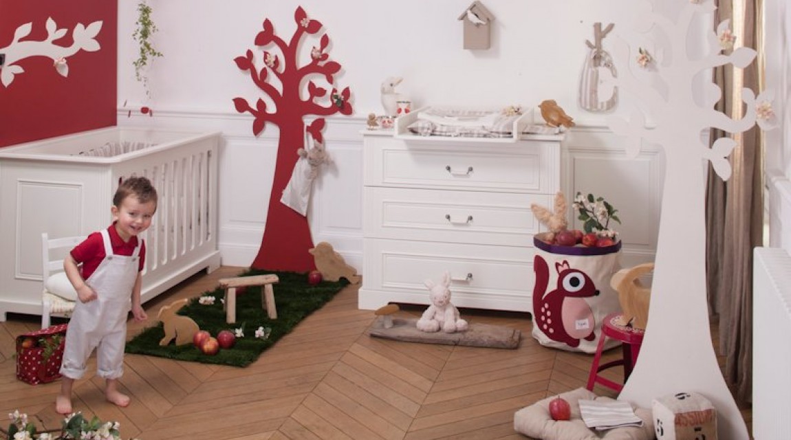 Pokój dziecięcy z biało - czerwonymi ścianami wyposażony w łóżeczko i komodę z przewijakiem