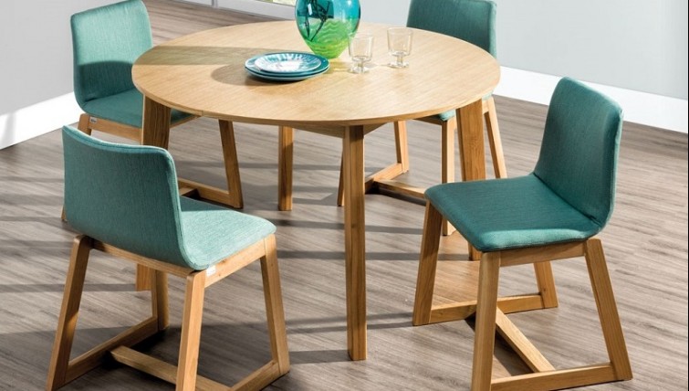 Rozkładany okrągły stół z fornirowanym blatem i zielone tapicerowane krzesła na drewnianych płozach