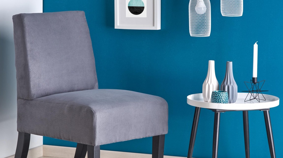 Tapicerowany fotel u boku białego stolika pomocniczego na tle niebieskiej i białej ściany w nowoczesnym salonie
