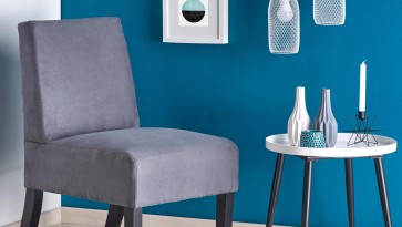 Tapicerowany fotel u boku białego stolika pomocniczego na tle niebieskiej i białej ściany w nowoczesnym salonie