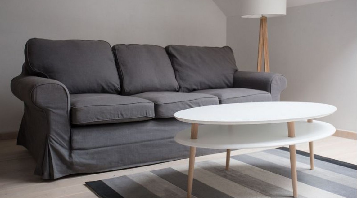 Owalny stolik z półką na drewnianych nogach w stylu skandynawskim jako uzupełnienie szarej sofy salonowej