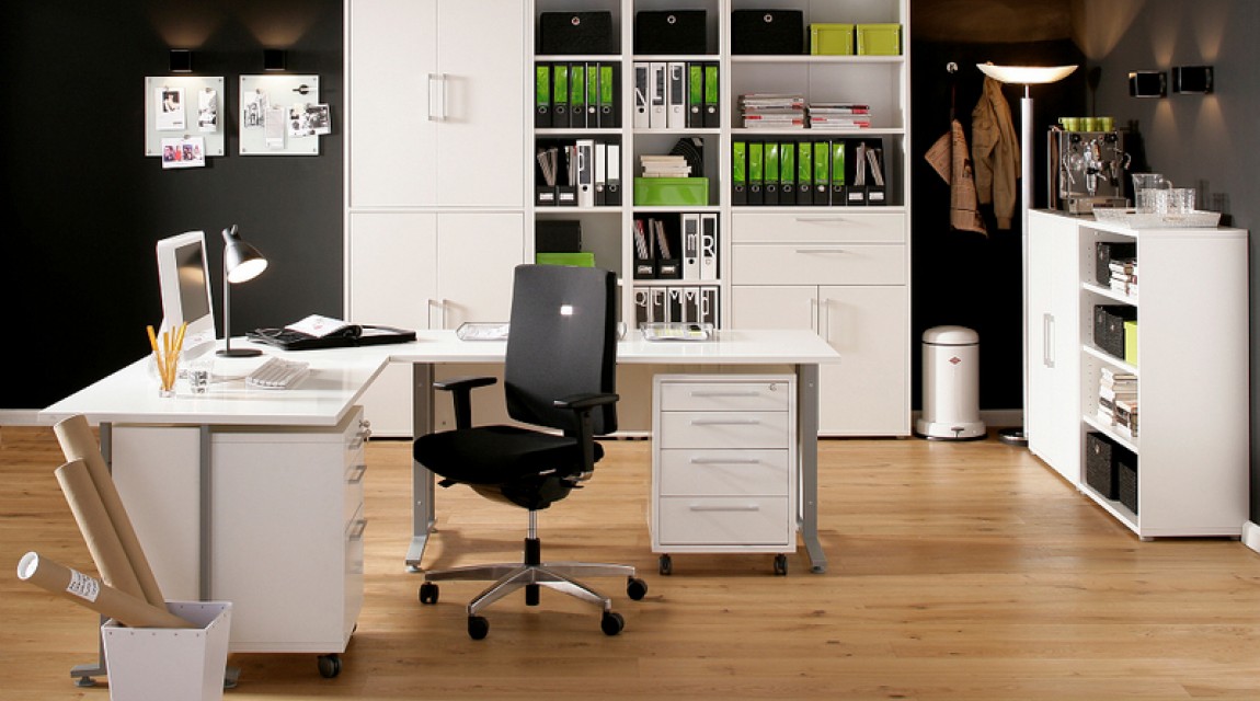Wnętrze gabinetowe z narożnym białym biurkiem oraz kontenerkiem z szufladami na kółkach