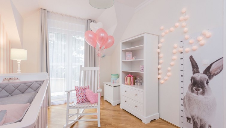Dziewczęcy pokój z różowymi dodatkami wyposażony w bujany fotel do karmienia oraz skrzynię na zabawki