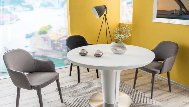 Okrągły stół z funkcją rozkładania na jednej nodze w zestawieniu z tapicerowanymi krzesłami w niewielkiej jadalni