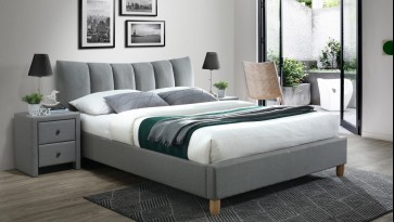 Tapicerowane łóżko na drewnianych nogach z wysokim zagłówkiem i szafka nocna z szufladami