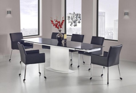 Stół z rozkładanym blatem i krzesłami na kółkach w nowoczesnej jadalni z modnym żyrandolem i oknami