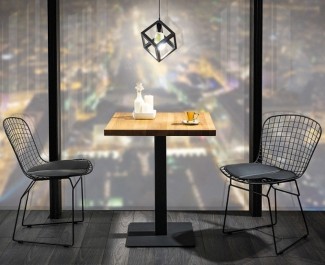 Drewniany stół na jednej nodze z kwadratowym blatem w zestawieniu z metalowymi krzesłami w jadani na tle dużego okna
